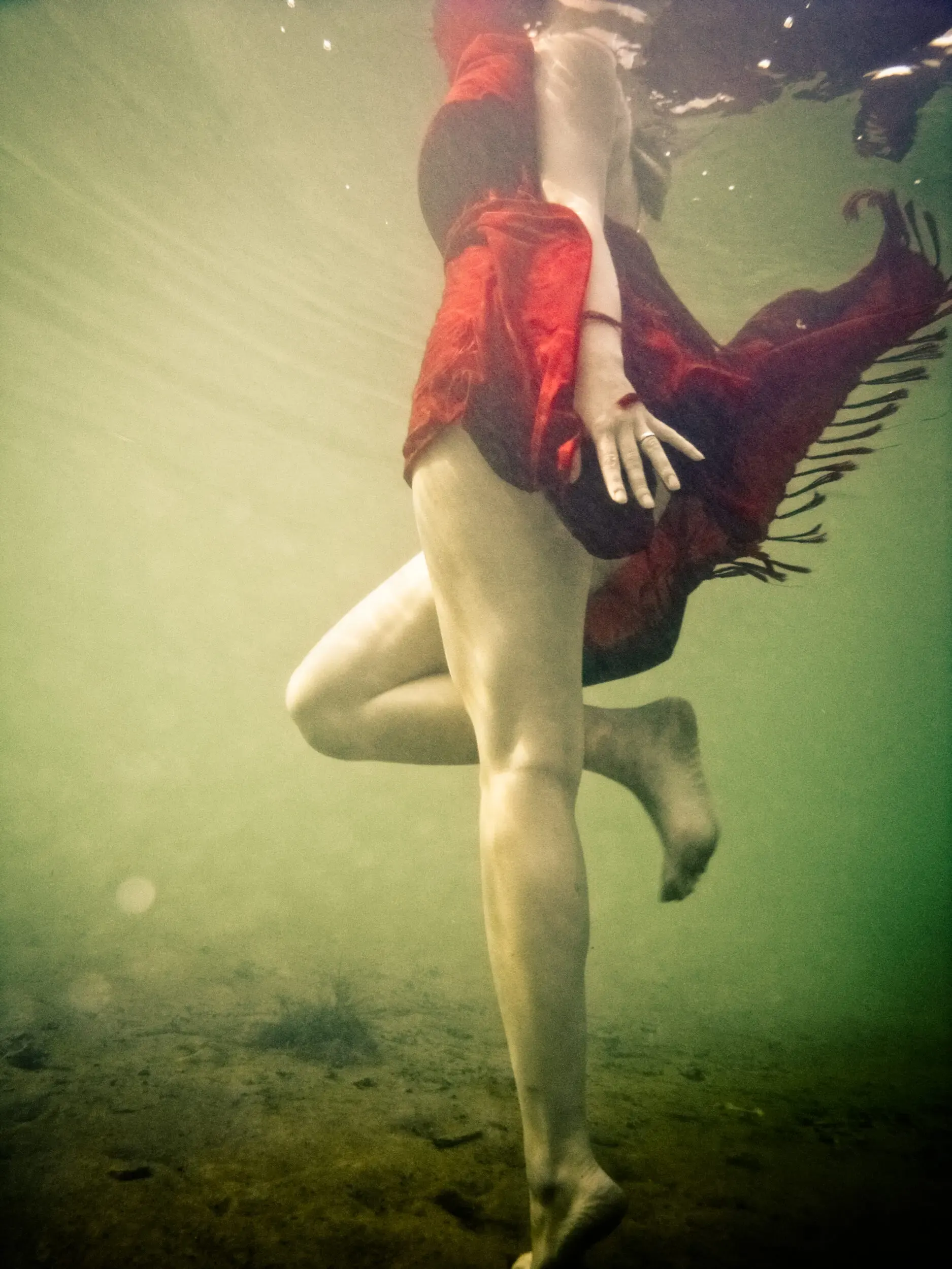 Frau in rotem Kleid schwebt unter Wasser im Sonnenlicht, under(water) love