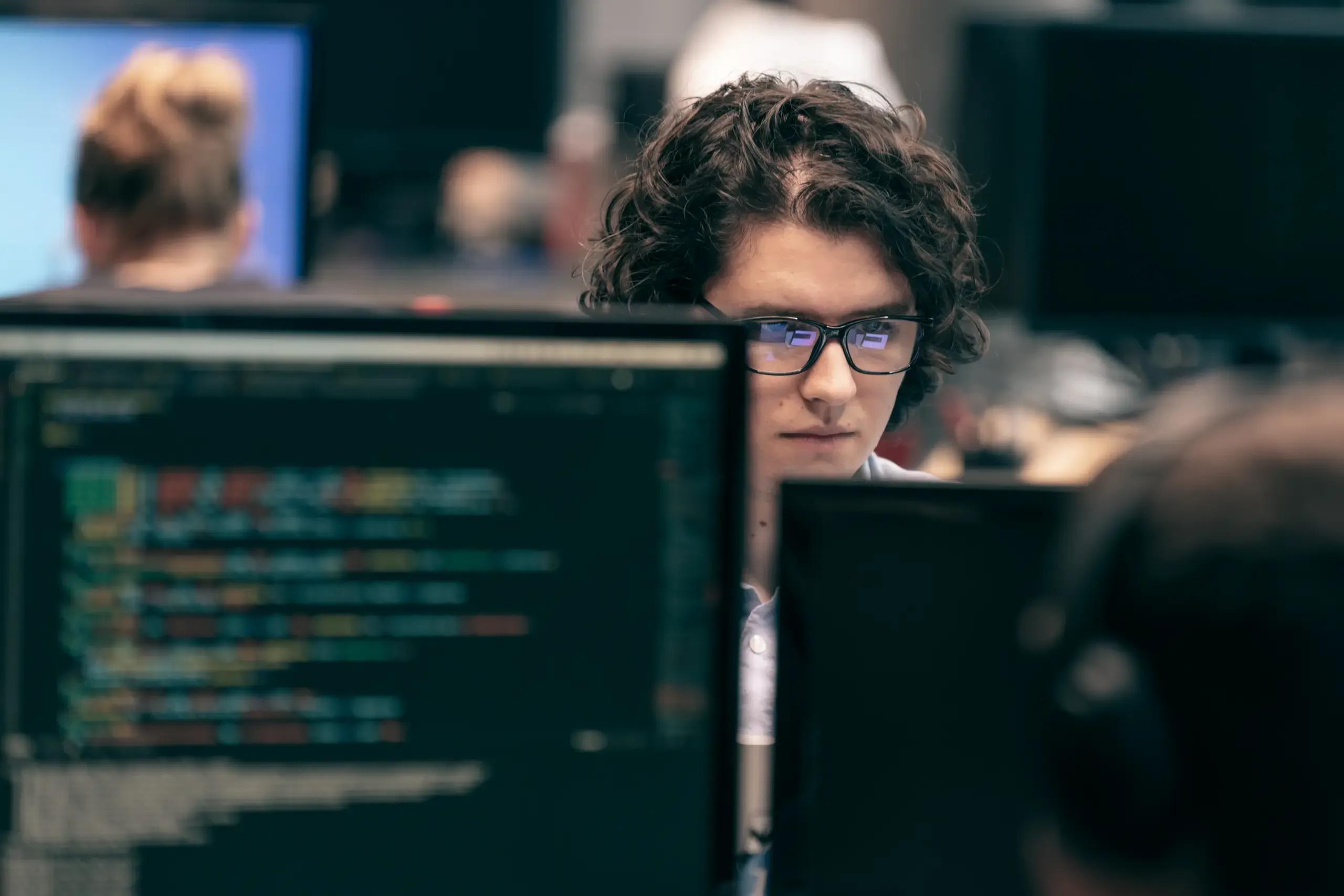 Junger Mann mit lockigem Haar und Brille blickt konzentriert auf Bildschirme mit Code, Verve Ventures