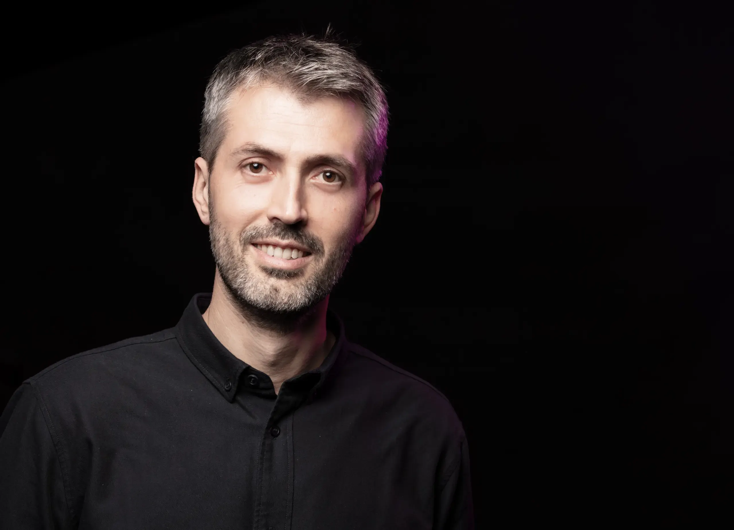 Portrait eines lächelnden Mannes im schwarzen Hemd vor dunklem Hintergrund, Verve Ventures