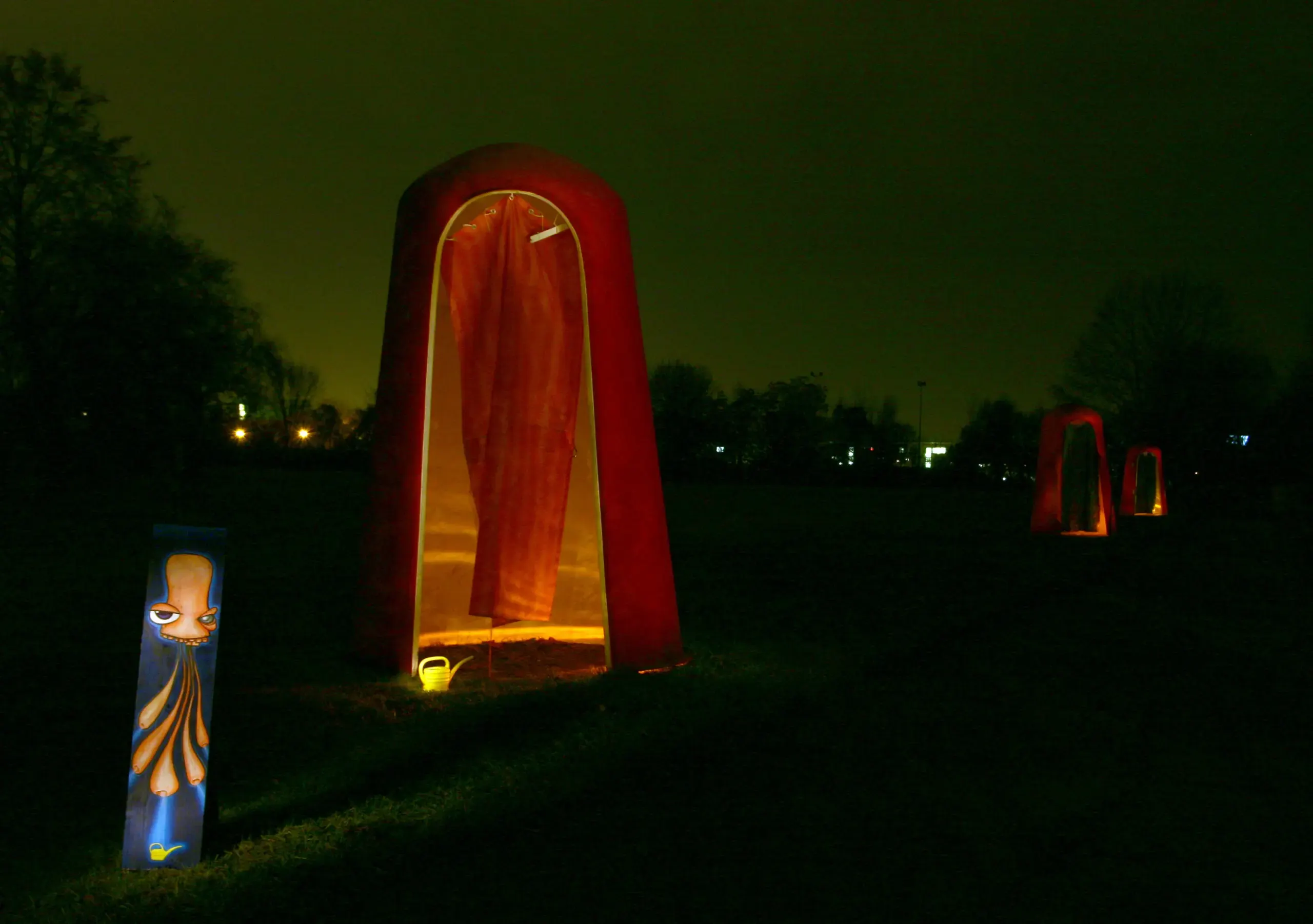 Hohe rot leuchtende Figur neben einer kleinen Can-Figur bei Nacht