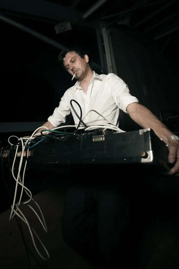 Man in a white shirt holding a large piece of equipment with multiple cables attached.